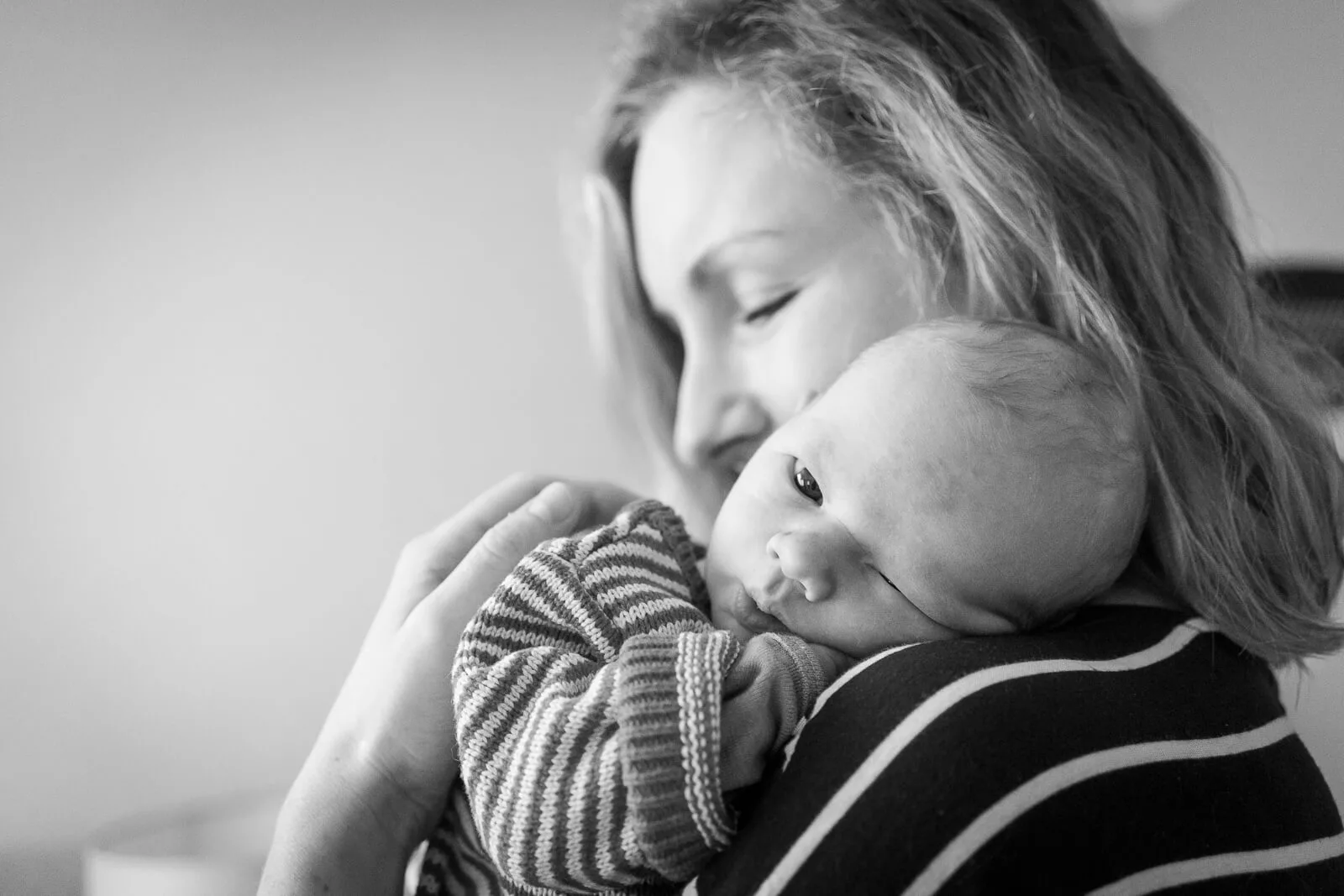 Eine Mutter trägt und kuschelt ihr Baby. Der Kopf des Babys liegt auf der Schulter der Mutter und die Mutter hat die Augen geschlossen. Das Foto ist schwarzweiß.