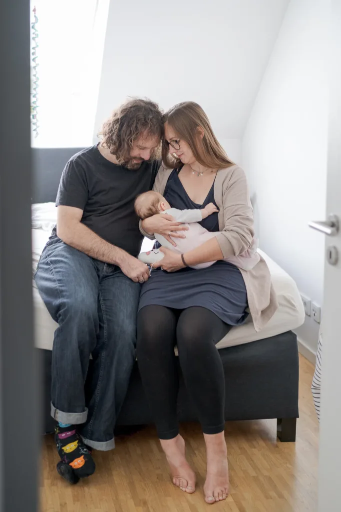 Ein Foto von einem Babyshooting. Zu ist eine Familie mit Vater, Mutter und Baby, welches gerade gestillt wird. Die Eltern lehnen die Köpfe aneinander, während die Mutter ihr Baby hält.