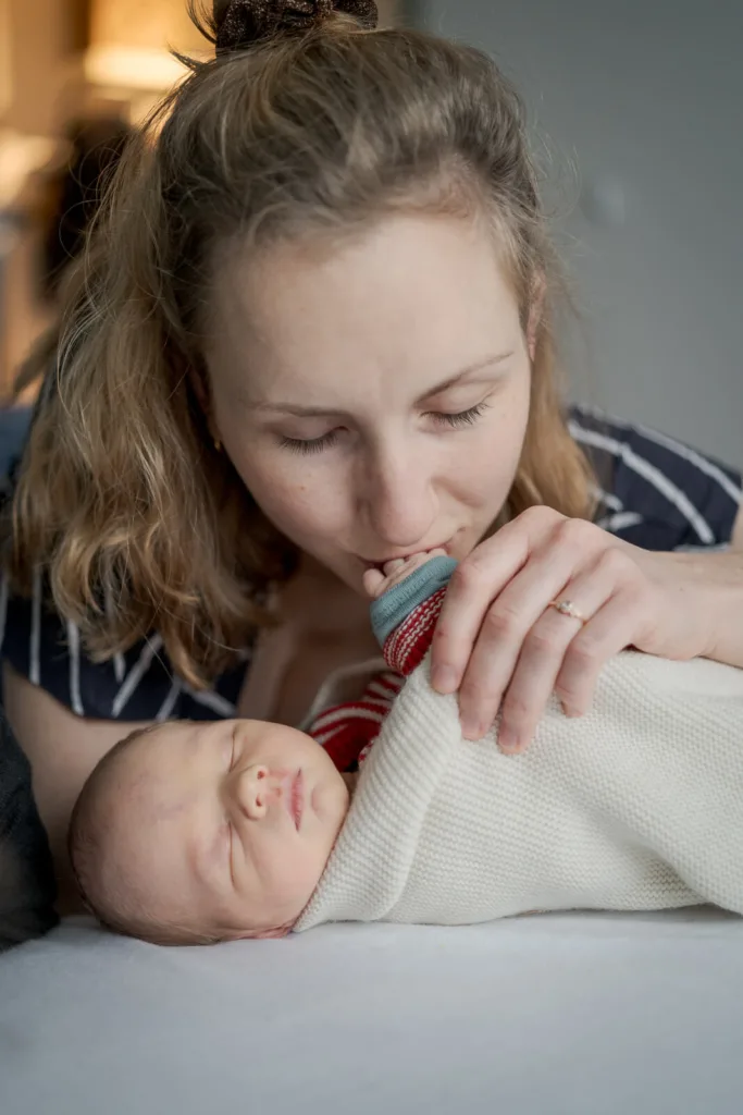 Ein Foto mit einer Mutter und ihrem Baby. Das Baby schläft. Die Mutter küsst das Händchen vom Baby.