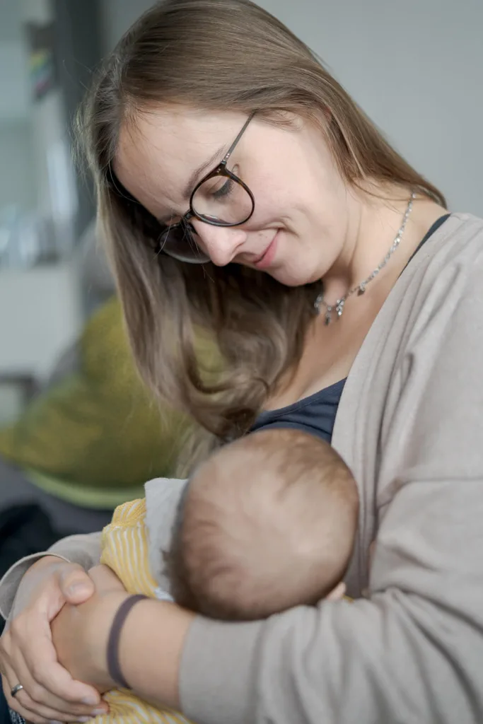 Die Eltern sitzen mit dem Baby im Bett während es gestillt wird.