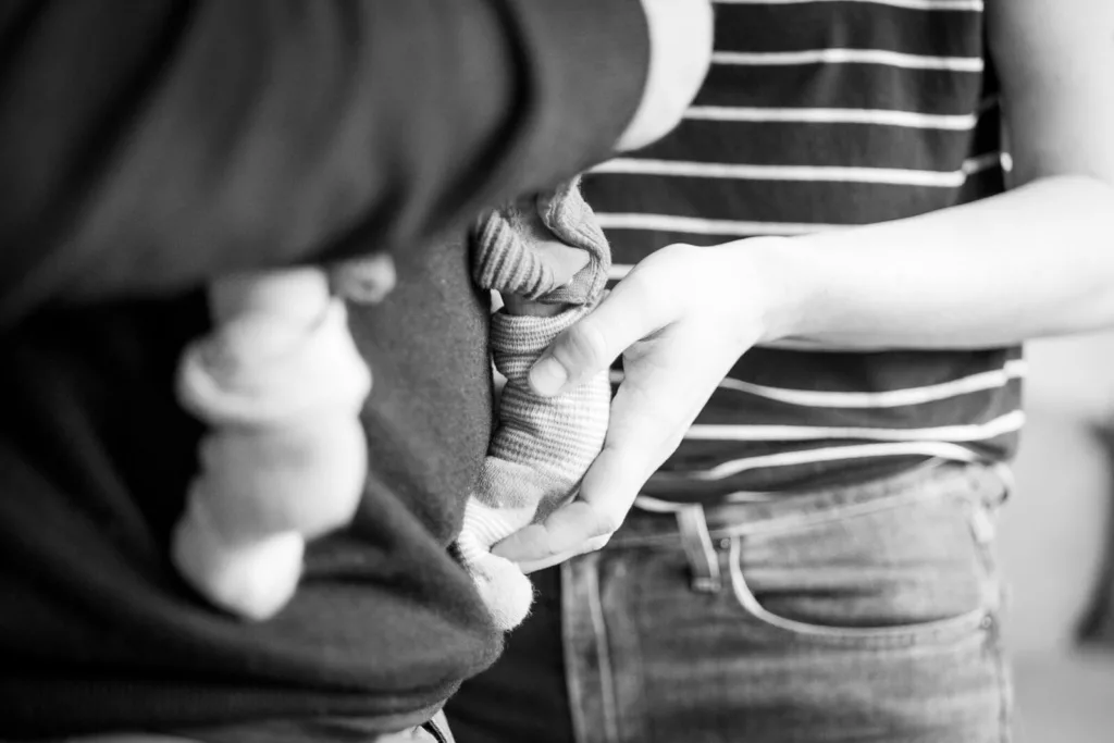 Ein Foto von einem Babyshooting. Es ist ein schwarz/weiß Foto. Zwei Eltern halten ihr Baby. Man sieht nur die Babyfüßchen, welches einer der Eltern hält.