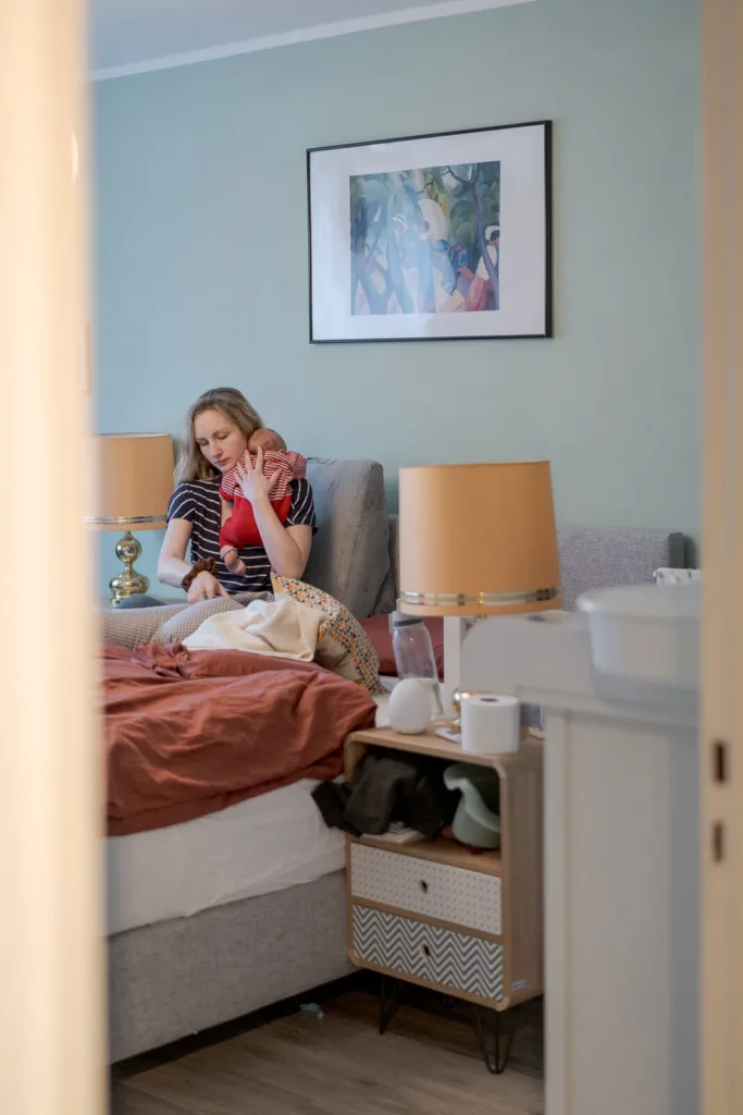 Ein Foto von einem Babyshooting. Zu sehen ist eine Mutter und Baby in einer Alltagssituation. Sie macht ihr Baby gerade fertig zum Stillen.