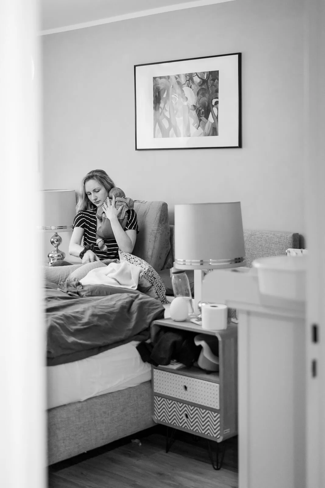 Ein Foto von einem Babyshooting. Zu sehen ist eine Mutter und Baby in einer Alltagssituation. Sie macht ihr Baby gerade fertig zum Stillen. Es ist ein schwarz/weiß Bild.